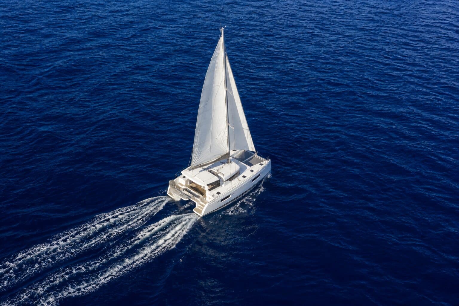 Sailing catamaran from above on deep blue water